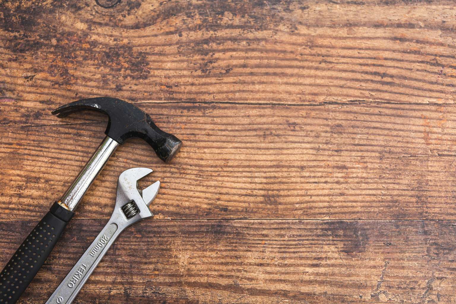 A claw hammer and adjustable wrench laid out on warm brown wood-grained floor planks