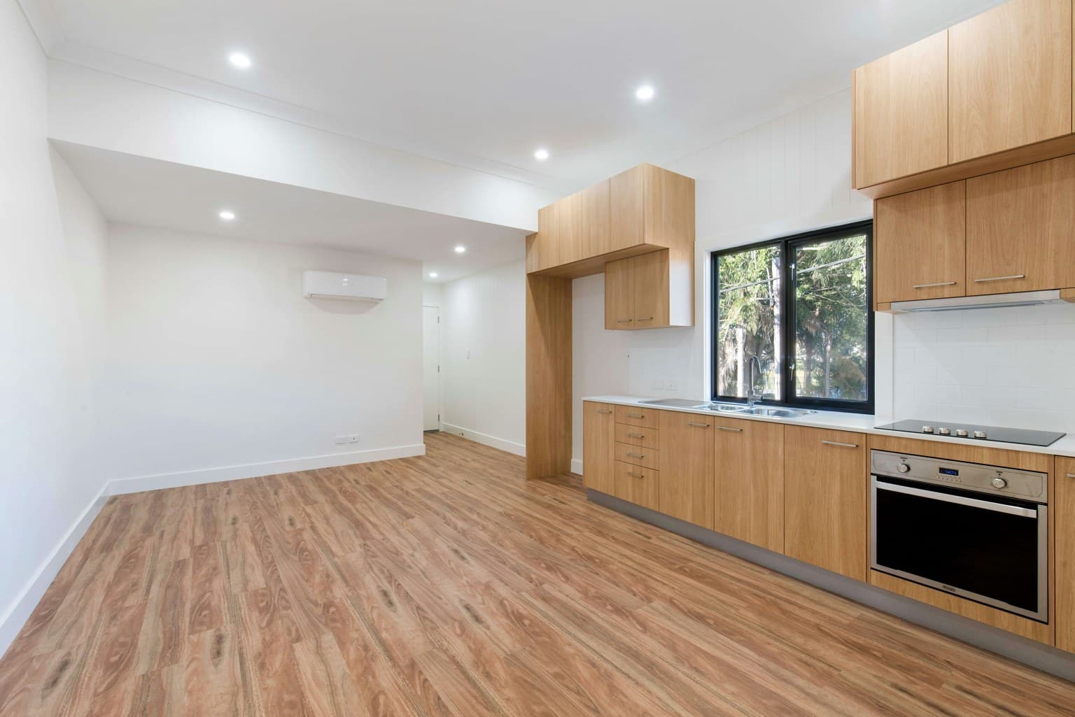A bright kitchen with wood-grain patterned flooring, wooden cabinetry, and a sink area with a window